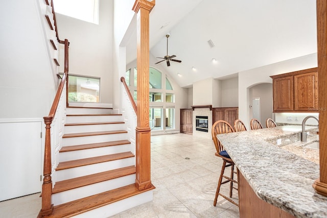 kitchen with high vaulted ceiling, light stone countertops, a kitchen bar, ceiling fan, and light tile floors