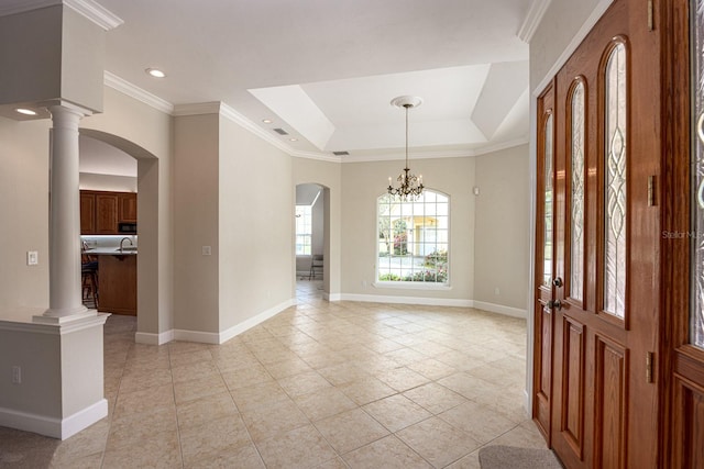 tiled foyer featuring a chandelier, crown molding, decorative columns, and a raised ceiling