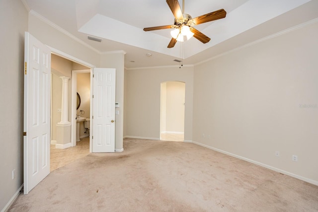 unfurnished bedroom featuring ceiling fan, a raised ceiling, light colored carpet, crown molding, and ornate columns