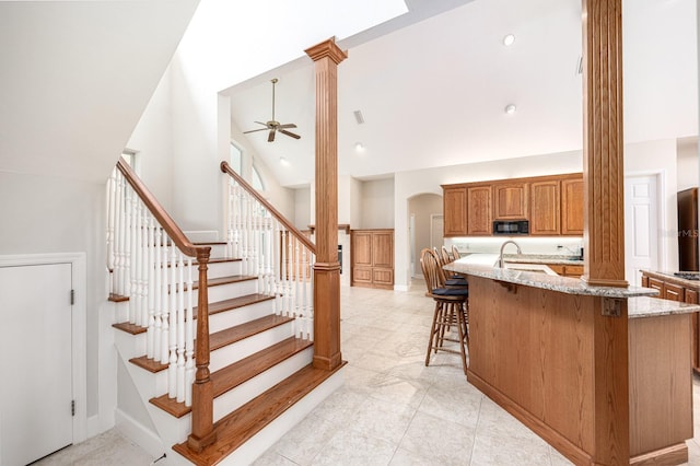 kitchen with light stone counters, ceiling fan, light tile floors, high vaulted ceiling, and a kitchen breakfast bar