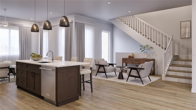 kitchen featuring sink, stainless steel dishwasher, decorative light fixtures, a kitchen island with sink, and light wood-type flooring