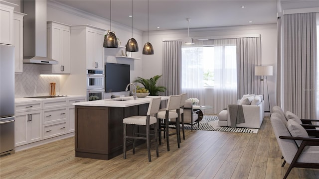 kitchen with a center island with sink, white cabinetry, sink, and wall chimney range hood