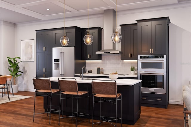 kitchen featuring a kitchen breakfast bar, wall chimney range hood, hanging light fixtures, and appliances with stainless steel finishes