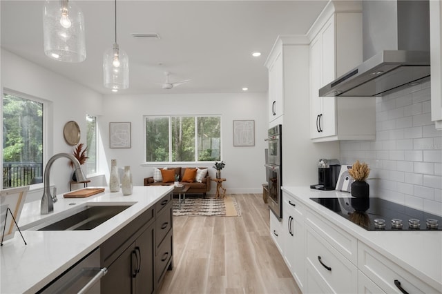 kitchen featuring sink, hanging light fixtures, wall chimney range hood, white cabinets, and plenty of natural light