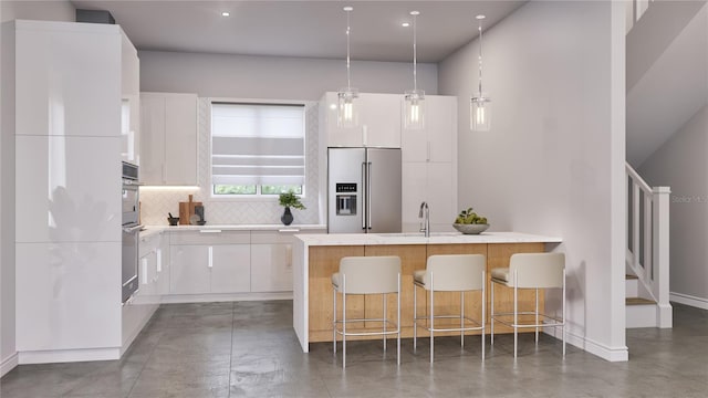 kitchen with a kitchen bar, appliances with stainless steel finishes, backsplash, white cabinetry, and hanging light fixtures