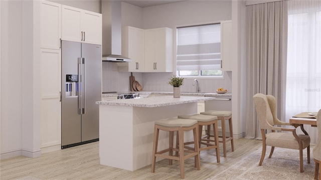 kitchen with appliances with stainless steel finishes, backsplash, wall chimney exhaust hood, light hardwood / wood-style flooring, and white cabinets