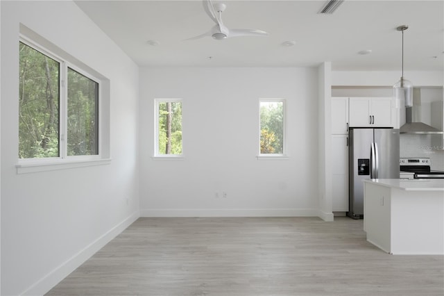 kitchen featuring ceiling fan, stainless steel appliances, wall chimney range hood, tasteful backsplash, and white cabinets