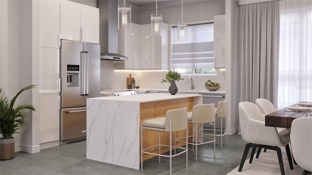 kitchen featuring wall chimney exhaust hood, high end refrigerator, white cabinets, pendant lighting, and backsplash