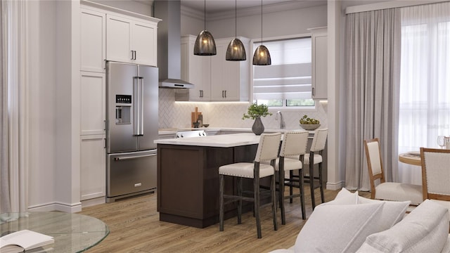 kitchen with high end fridge, decorative light fixtures, a kitchen island, white cabinets, and wall chimney range hood