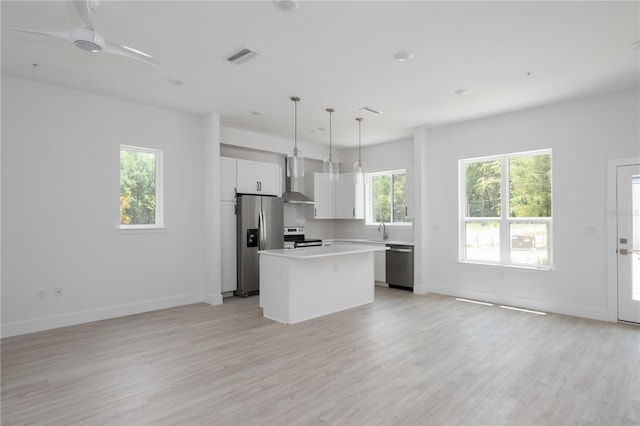 kitchen with appliances with stainless steel finishes, decorative light fixtures, white cabinetry, a center island, and wall chimney range hood