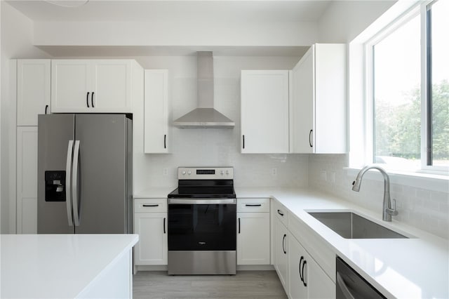 kitchen with appliances with stainless steel finishes, sink, white cabinets, decorative backsplash, and wall chimney range hood