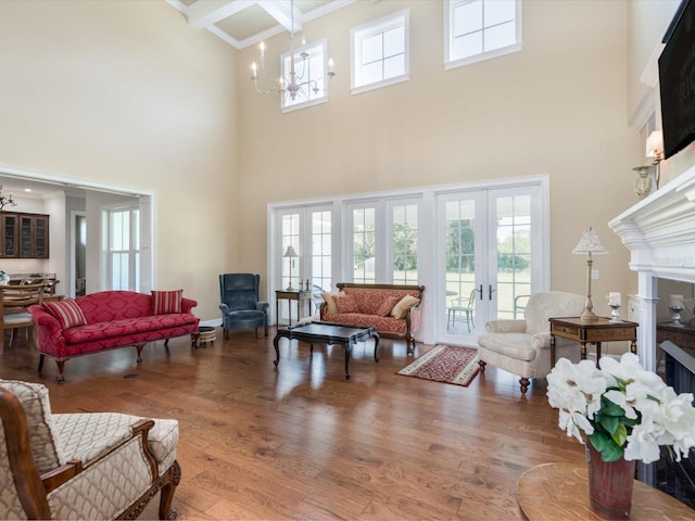 living room featuring french doors, a tile fireplace, a towering ceiling, hardwood / wood-style floors, and a chandelier