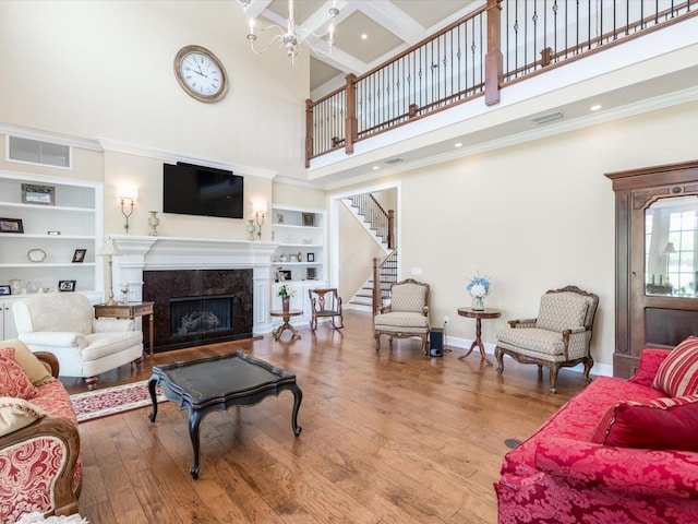 living room with light hardwood / wood-style floors, a high ceiling, a premium fireplace, crown molding, and built in features