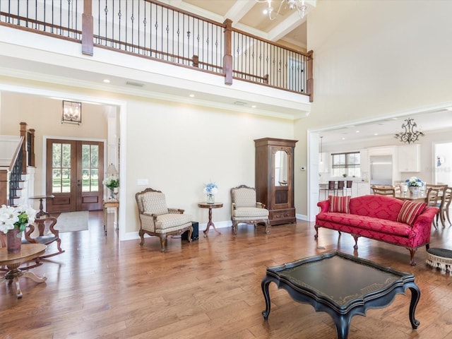 living room featuring a high ceiling, a notable chandelier, light hardwood / wood-style floors, and french doors