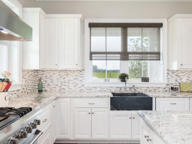 kitchen with backsplash, wall chimney exhaust hood, white cabinets, and sink