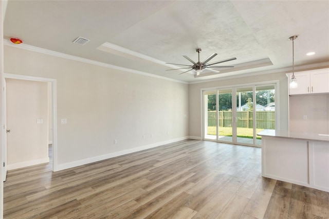 unfurnished living room featuring a raised ceiling, ornamental molding, ceiling fan, and light hardwood / wood-style flooring