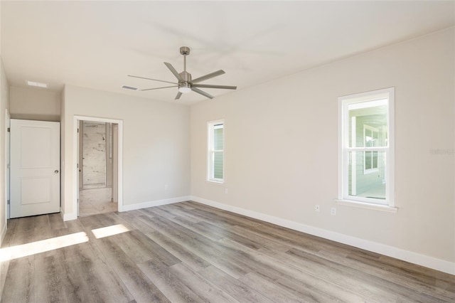 unfurnished bedroom with multiple windows, ensuite bath, ceiling fan, and light hardwood / wood-style floors