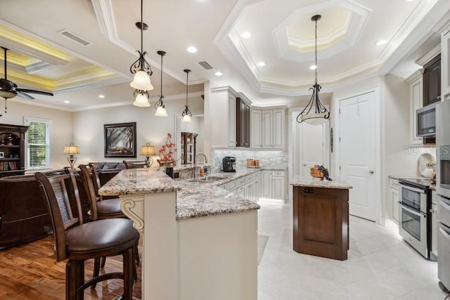 kitchen with pendant lighting, a tray ceiling, sink, and a kitchen breakfast bar