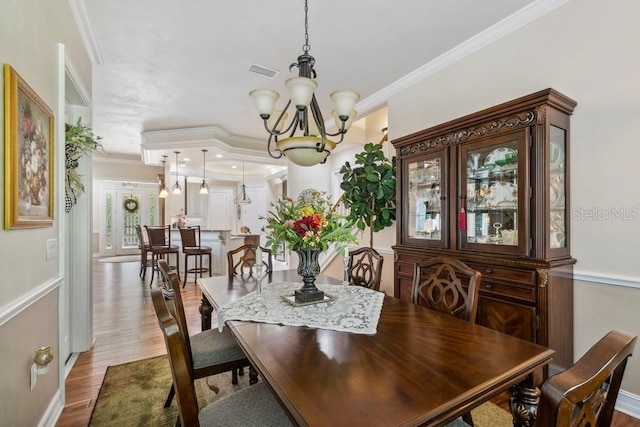 dining space featuring wood-type flooring, a notable chandelier, and ornamental molding