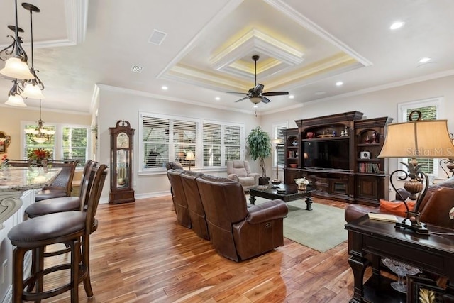 living room featuring ceiling fan with notable chandelier, a raised ceiling, light wood-type flooring, and ornamental molding