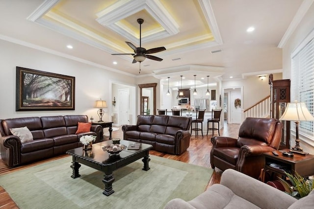 living room with ceiling fan, a tray ceiling, ornamental molding, and light hardwood / wood-style flooring