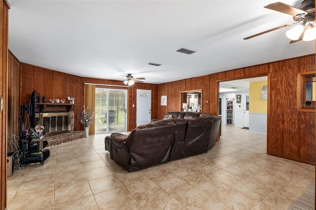 living room featuring wooden walls, ceiling fan, and a brick fireplace