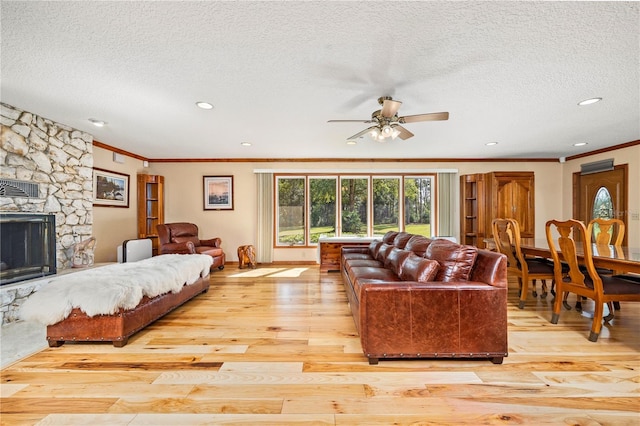 living room with a textured ceiling, a stone fireplace, ceiling fan, and light wood-type flooring