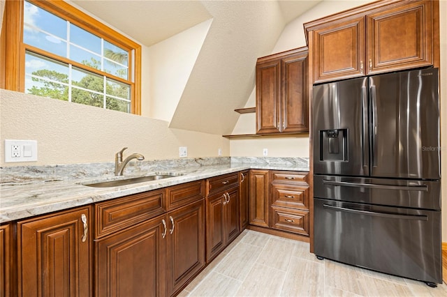 kitchen featuring stainless steel fridge, sink, light tile floors, light stone counters, and vaulted ceiling