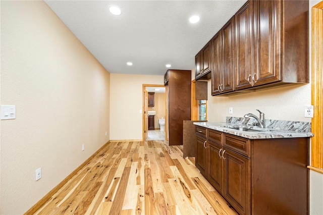 kitchen with dark brown cabinetry, sink, and light wood-type flooring