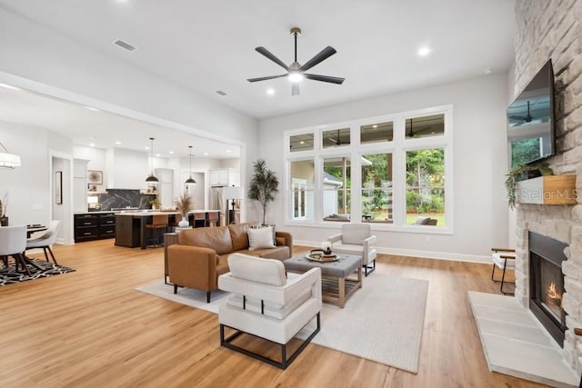 living room featuring a fireplace, light wood-type flooring, and ceiling fan