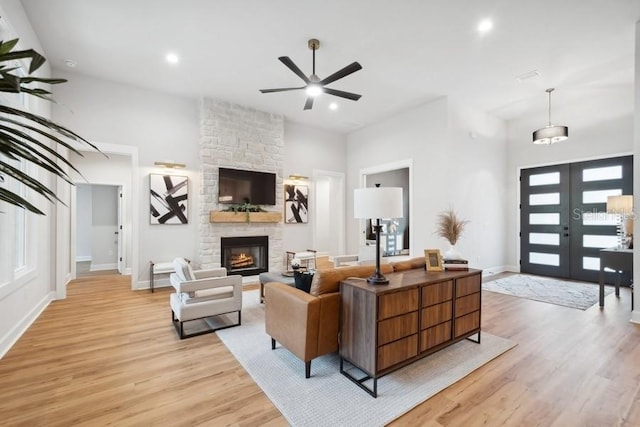 living room featuring ceiling fan, french doors, light hardwood / wood-style floors, and a stone fireplace