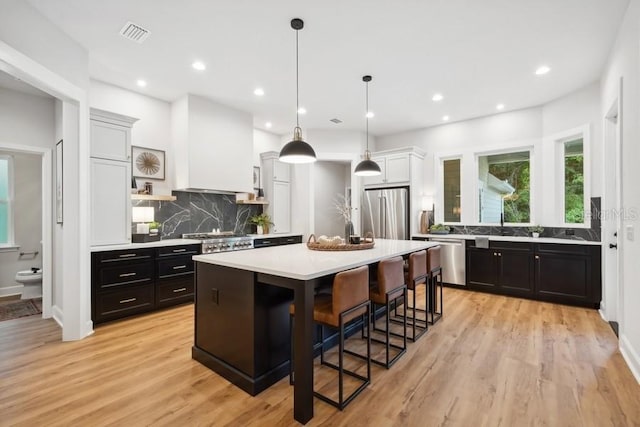 kitchen featuring light hardwood / wood-style floors, custom exhaust hood, a kitchen island, a breakfast bar, and appliances with stainless steel finishes