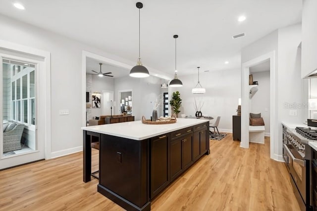 kitchen with light hardwood / wood-style flooring, pendant lighting, a center island, high end stainless steel range oven, and ceiling fan