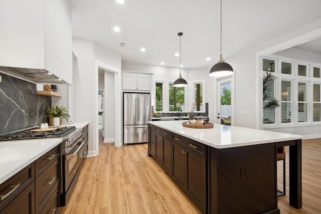 kitchen featuring appliances with stainless steel finishes, light hardwood / wood-style floors, pendant lighting, white cabinets, and tasteful backsplash