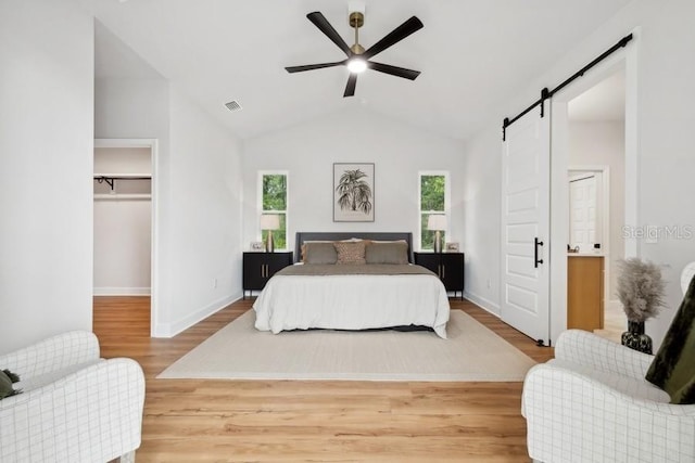 bedroom featuring ceiling fan, a walk in closet, a barn door, and wood-type flooring