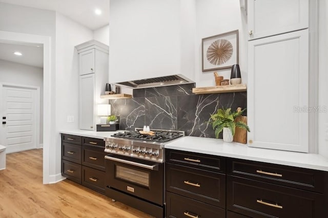 kitchen with white cabinets, light hardwood / wood-style floors, backsplash, and high end stainless steel range oven