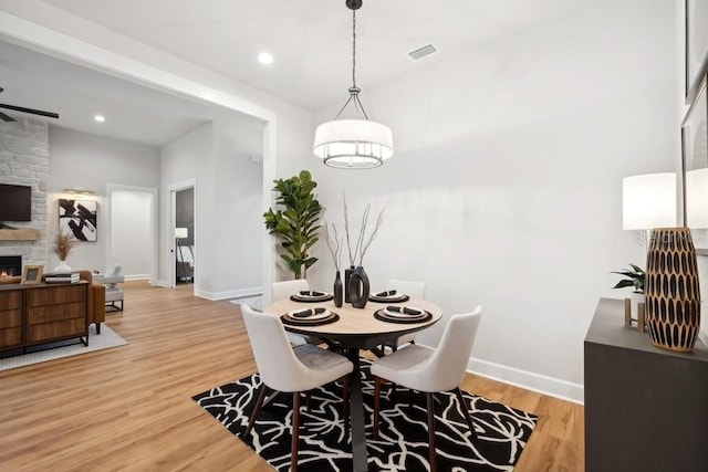 dining area with a fireplace, light wood-type flooring, and ceiling fan