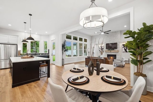 dining area featuring a fireplace, ceiling fan, and light wood-type flooring