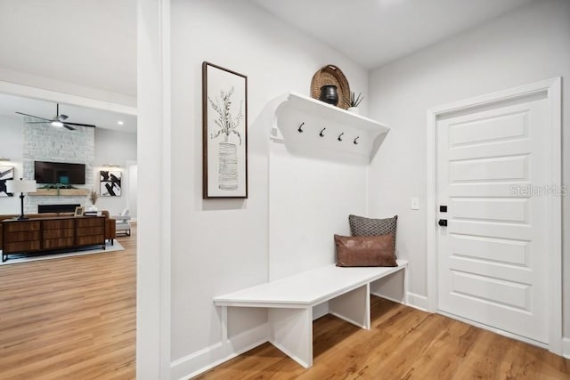 mudroom featuring a fireplace, light wood-type flooring, and ceiling fan