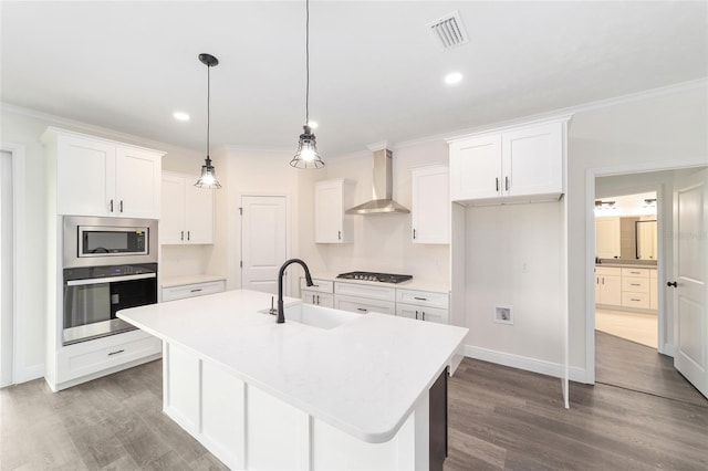 kitchen with dark hardwood / wood-style floors, a kitchen island with sink, appliances with stainless steel finishes, sink, and wall chimney range hood