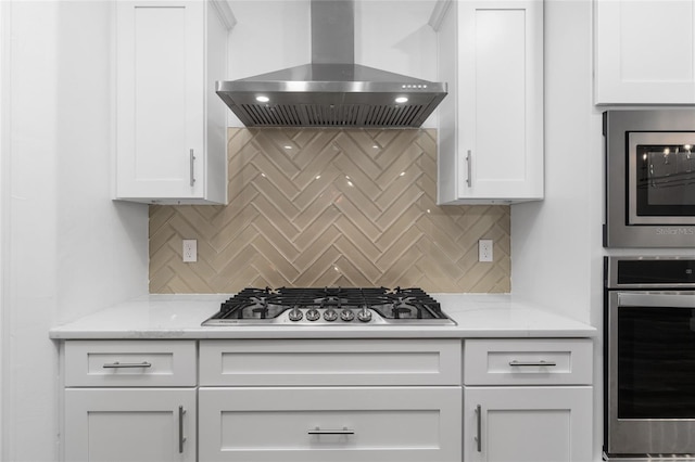 kitchen featuring appliances with stainless steel finishes, white cabinetry, backsplash, and wall chimney range hood