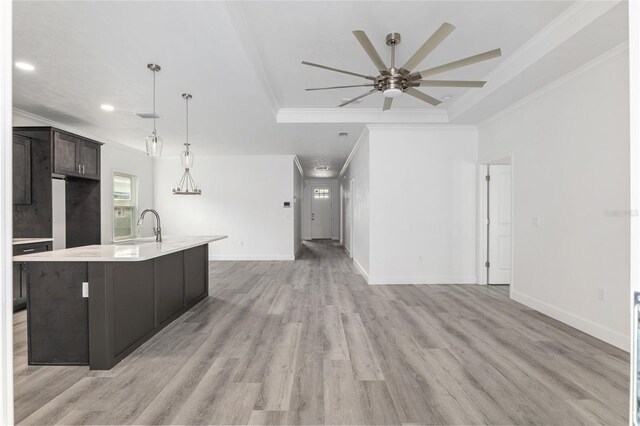 kitchen featuring a kitchen island with sink, ceiling fan, pendant lighting, a raised ceiling, and light hardwood / wood-style flooring