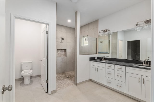 bathroom with double sink, a tile shower, tile floors, vanity with extensive cabinet space, and toilet