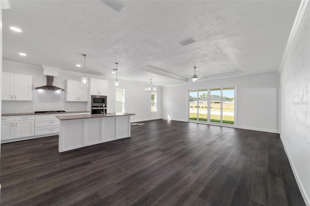 kitchen featuring wall chimney exhaust hood, a center island with sink, pendant lighting, stainless steel appliances, and white cabinets