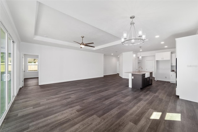 unfurnished living room featuring sink, a tray ceiling, dark hardwood / wood-style flooring, and ceiling fan with notable chandelier