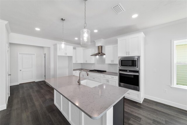 kitchen with white cabinetry, hanging light fixtures, stainless steel appliances, a center island with sink, and wall chimney exhaust hood