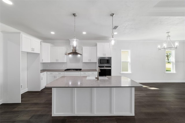 kitchen featuring stainless steel appliances, white cabinetry, hanging light fixtures, and a kitchen island with sink