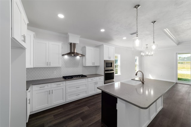 kitchen featuring wall chimney exhaust hood, sink, stainless steel appliances, a kitchen island with sink, and white cabinets