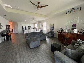 living room with track lighting, a tray ceiling, ceiling fan, and dark hardwood / wood-style flooring