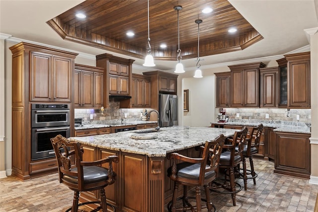 kitchen featuring appliances with stainless steel finishes, a tray ceiling, a breakfast bar area, and a center island with sink